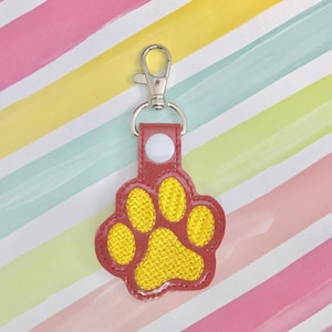 Op de afbeelding: Sleutelhanger in de vorm van een rode en gele poot met een zilveren metalen sluiting.