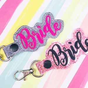 May include: Two silver and pink glitter keychains with the word "Bride" in pink and black lettering.