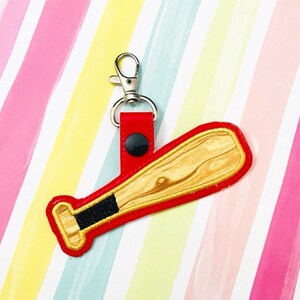 May include: A red and brown baseball bat keychain with a silver clip. The bat has a wood grain pattern.