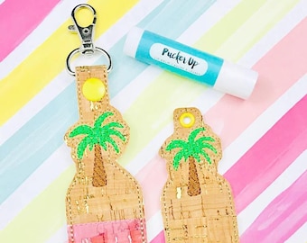 Puede incluir: Dos llaveros de corcho y tela con un diseño de palmera. El llavero de la izquierda tiene una inserción de tela rosa. El llavero de la derecha es de color corcho sólido. Los llaveros están sobre un fondo a rayas.