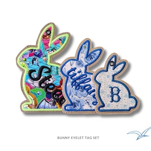 May include: Three bunny-shaped eyelet tags in varying sizes. The largest features a colorful stained-glass design with the name "S", the middle one has a blue floral pattern with the name "Tiffany", and the smallest has a blue floral pattern with the letter "B".