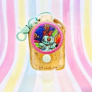 May include: A light blue and pink hand sanitizer holder with a cork exterior and a round, pink-trimmed patch featuring a cartoon character with blue and green colors. The holder has a light blue carabiner clip.