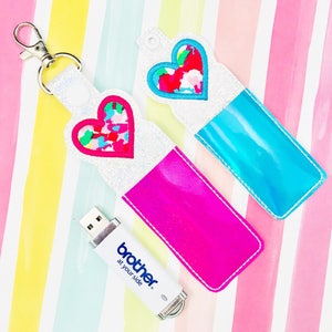 May include: Two keychains with heart-shaped designs and a USB drive. One keychain is hot pink, the other is blue. The hearts have colorful confetti-like patterns. The USB drive is white with the text "brother at your side."