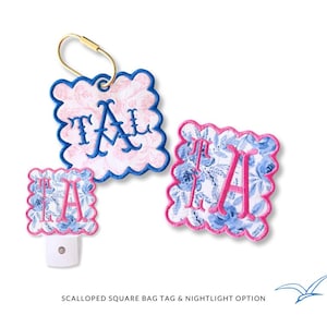 May include: A collection of personalised items: a scalloped square bag tag with a gold clasp, a nightlight, and a matching tag. Each item features a floral pattern with blue flowers, pink trim, and the embroidered letters "TA" in blue or pink.
