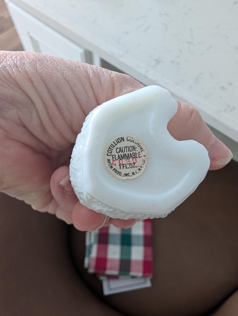 K&ouml;nnte beinhalten: Eine wei&szlig;e, strukturierte Parf&uuml;mflasche mit einem Aufkleber mit der Aufschrift "Cotillion Cologne" und "Vorsicht: Entz&uuml;ndlich". Die Flasche wird in einer Hand gehalten. Die Flasche enth&auml;lt 29,57 ml.