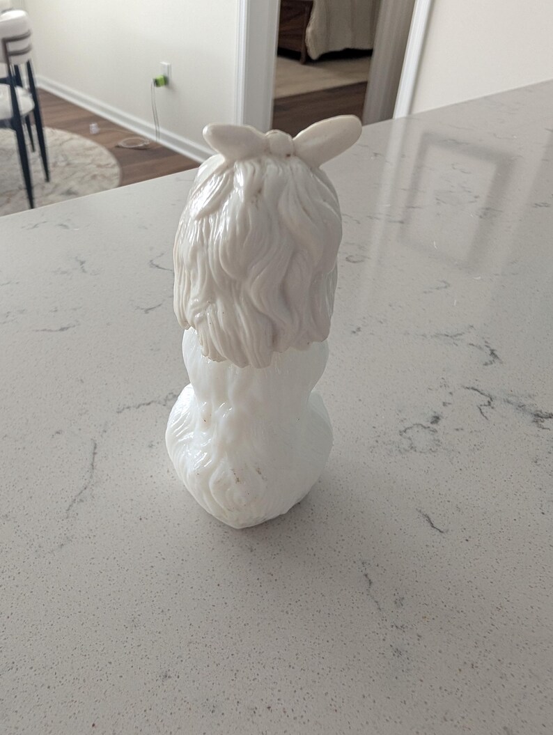 K&ouml;nnte beinhalten: Eine wei&szlig;e Keramikfigur einer Frau mit einer Schleife im Haar. Die Figur hat eine detaillierte Frisur und einen abgerundeten Sockel. Das Gesamtdesign ist glatt und elegant, mit gl&auml;nzendem Finish.