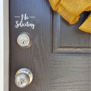 May include: A dark gray front door with a silver door knob and deadbolt lock. A sign on the door reads "No Soliciting".
