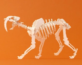 May include: White paper model of a saber-toothed cat skeleton. The model is posed in a walking position with its mouth open and fangs visible.