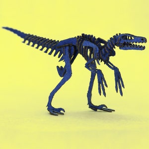 May include: A blue cardboard model of a dinosaur skeleton. The dinosaur is standing on a yellow surface.
