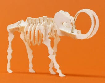 May include: A white cardboard model of a mammoth skeleton. The model is posed standing with its legs spread apart and its trunk raised. The model is detailed with ribs, vertebrae, and leg bones.