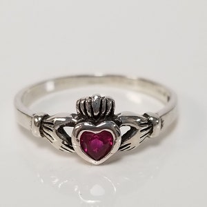 Könnte beinhalten: Ein silberner Ring mit einem herzförmigen Rubin, der in einem keltischen Knotendesign eingefasst ist.