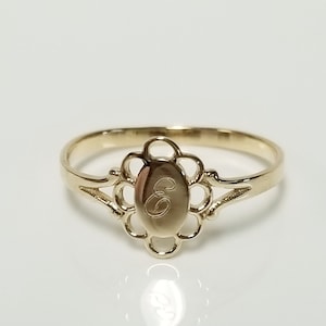 May include: A gold ring featuring a delicate floral design and an oval-shaped centrepiece engraved with the letter "E".