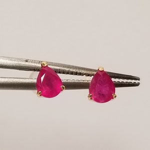 May include: A pair of gold earrings with pear-shaped red ruby gemstones.