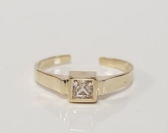 May include: A gold ring with a square-shaped clear stone set in the center.