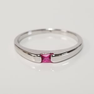 May include: A silver band ring with a single, small, rectangular, pink gemstone.