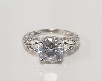 May include: A silver ring with a large, clear, round gemstone set in a delicate, ornate filigree design.