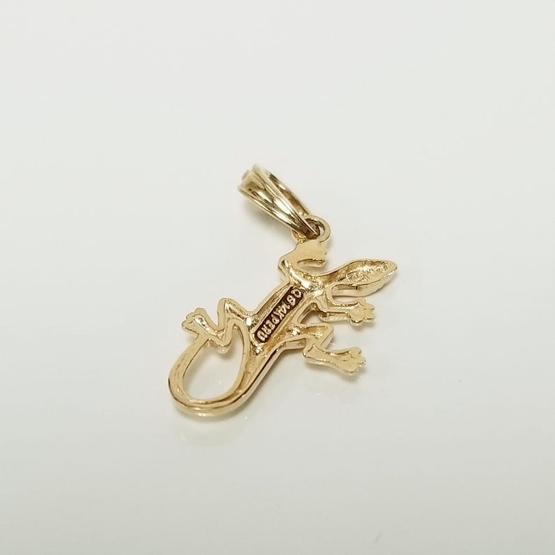 May include: Gold-toned pendant charm in the shape of a lizard. The back of the charm is engraved with the text "925 ITALY".