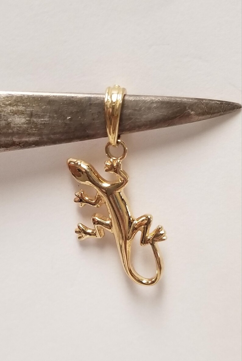 May include: A gold-toned lizard pendant charm with a detailed design. The pendant has a loop at the top for attaching to a chain or bracelet.