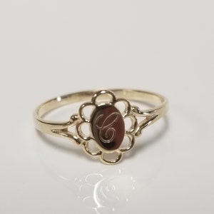 May include: A gold ring featuring a delicate floral design and an oval-shaped centrepiece engraved with the letter "C".