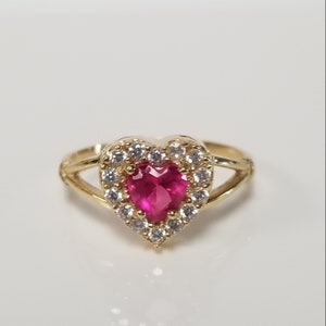 May include: A gold ring with a heart-shaped pink gemstone surrounded by a halo of smaller white gemstones.