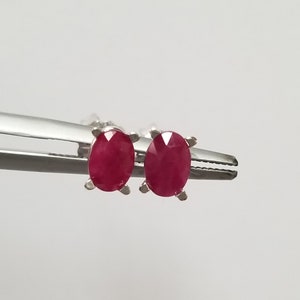 May include: A pair of silver stud earrings with oval-shaped ruby gemstones.