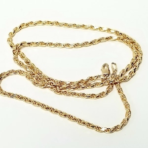 May include: A gold-colored rope chain necklace featuring a twisted, textured link design. The chain is arranged in a loose, overlapping loop and includes a small, functional lobster claw clasp mechanism at one end for secure fastening.