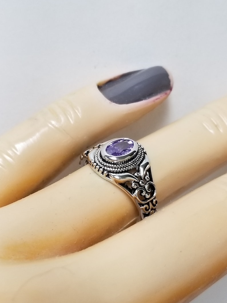 May include: A silver ring with an oval-shaped purple gemstone set in a filigree design.