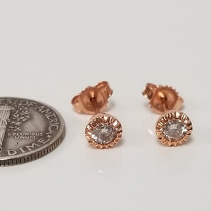 May include: A pair of rose gold stud earrings with a small round clear stone in the center of each earring.
