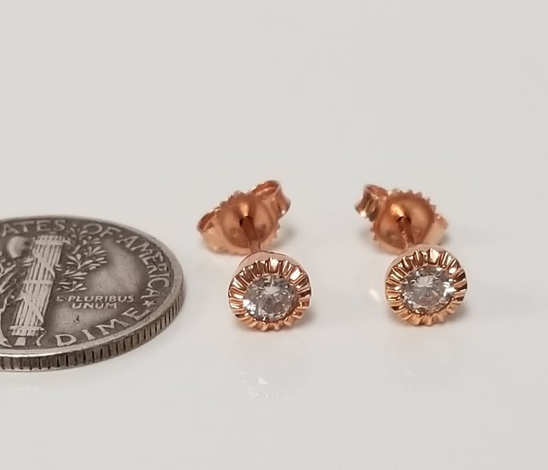 May include: A pair of rose gold stud earrings with a small round clear stone in the center of each earring.