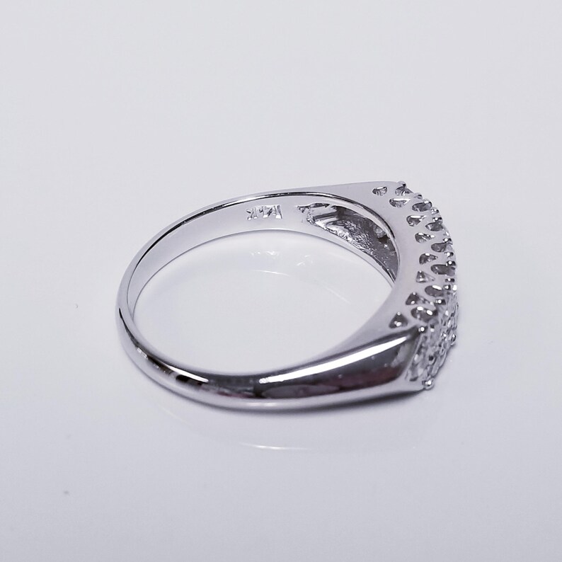 Op de afbeelding: Een zilveren bandring met een rij kleine, heldere stenen die in een gebogen ontwerp zijn gezet. De ring is aan de binnenkant gemarkeerd met het nummer "14K".