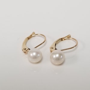 May include: A pair of gold-toned earrings with a single white pearl on each earring.