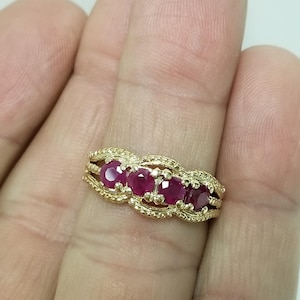 May include: A gold ring with five red gemstones. The ring has an intricate, filigree pattern around the stones. The gemstones are set in a row, creating a classic and eye-catching piece of jewellery. The ring's design is detailed and ornate.