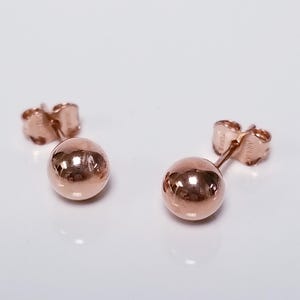 May include: A pair of rose gold ball stud earrings. The earrings are simple and elegant, and they would make a great gift for any occasion.