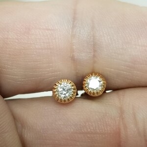 May include: A pair of gold stud earrings with a single round diamond in each setting.