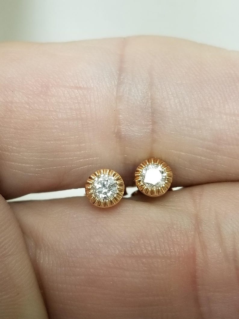 May include: A pair of gold stud earrings with a single round diamond in each setting.