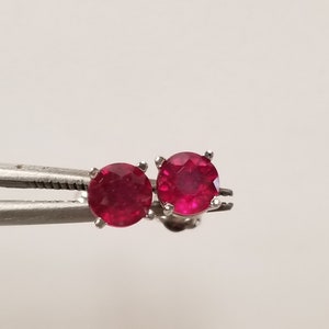 May include: A pair of silver stud earrings with round, red ruby gemstones.