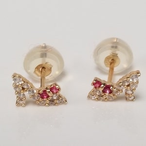 May include: A pair of gold earrings shaped like high heels with clear and red cubic zirconia stones.