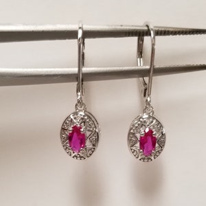 May include: A pair of silver dangle earrings featuring a pink oval gemstone surrounded by smaller clear gemstones.