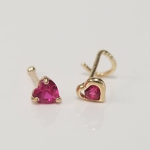 May include: Two gold nose rings with a heart-shaped setting and a pink gemstone.