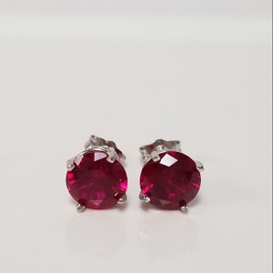 May include: A pair of silver stud earrings with round, bright red ruby gemstones.