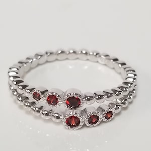 May include: A silver ring with a double band of small beads and five red gemstones.