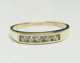 May include: A gold band ring featuring a channel setting with five small, clear, round-cut stones arranged horizontally across the front. The interior of the band is engraved with the text NG 10K, indicating the metal purity and hallmark.