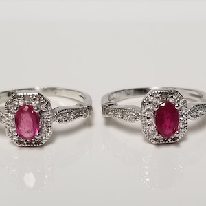 May include: Two silver rings with oval-shaped red gemstones surrounded by smaller white gemstones.