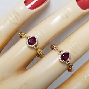 May include: Two gold rings with red gemstones and diamond accents. The rings are on a mannequin hand.