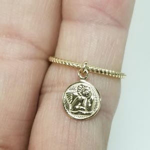 May include: A gold ring with a twisted band and a small charm of an angel with wings.