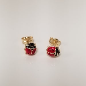 May include: A pair of gold ladybug earrings with red and black enamel. The earrings are small and delicate, perfect for everyday wear.