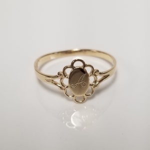 May include: A gold ring with a delicate floral design and an oval-shaped centre featuring the letter "A" engraved inside.