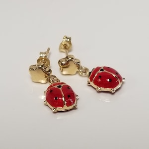 May include: Gold ladybug earrings with red enamel and black spots. The earrings have a star-shaped dangle.