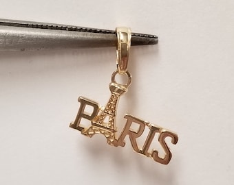 May include: Gold charm pendant featuring the Eiffel Tower and the word "PARIS" in a stylized font.