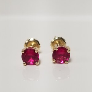 Könnte beinhalten: Ein Paar goldene Ohrstecker mit roten Rubin-Edelsteinen.